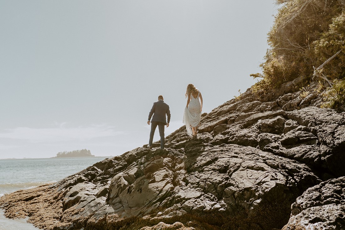 Adventurous eloping couple climb up rock face of cliff on Tofino beach