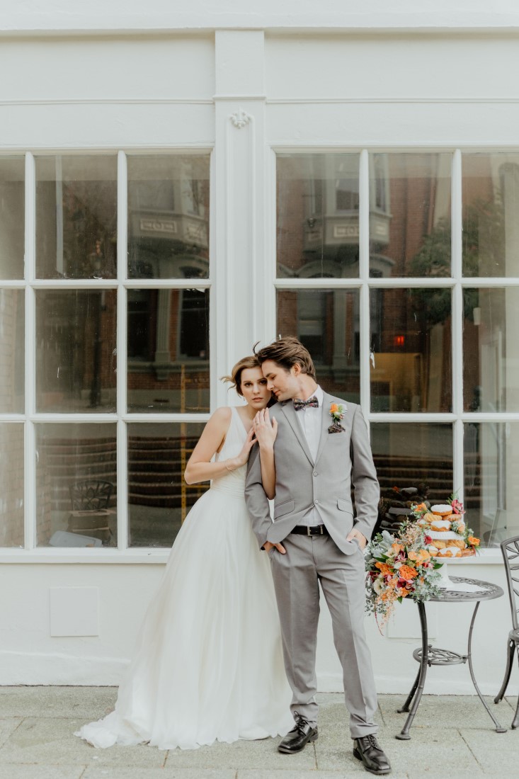 Coffee Love in Comox Valley Luke Liable Photography couple stands beside cafe table with donuts and bridal bouquet