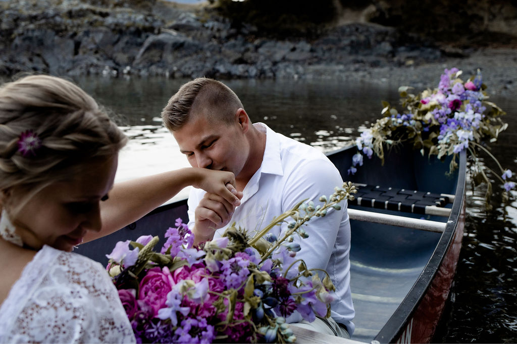 Groom kisses brides hand while sitting in a canoe on Vancouver Island
