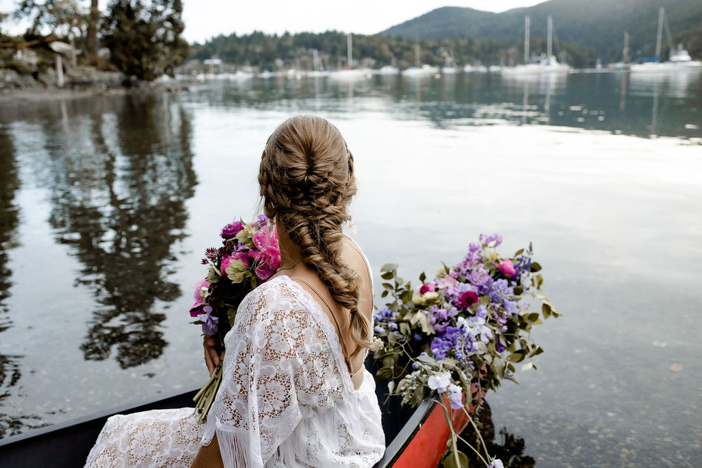 Bride with wedding day braid in her hair sits in canoe with flowers
