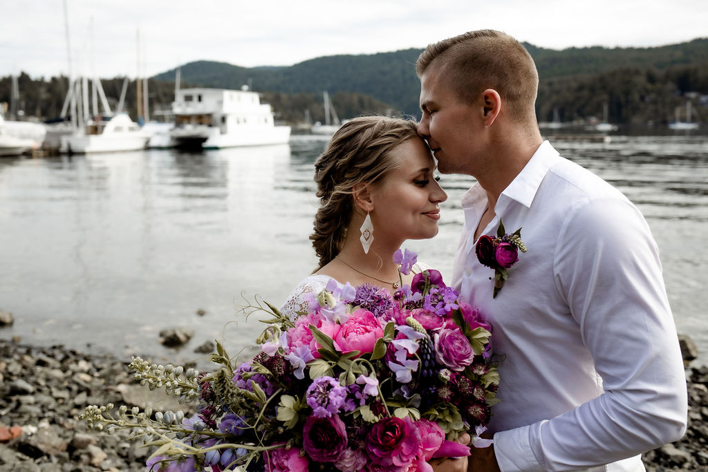 Newlyweds kiss with boat behind them on Vancouver Island
