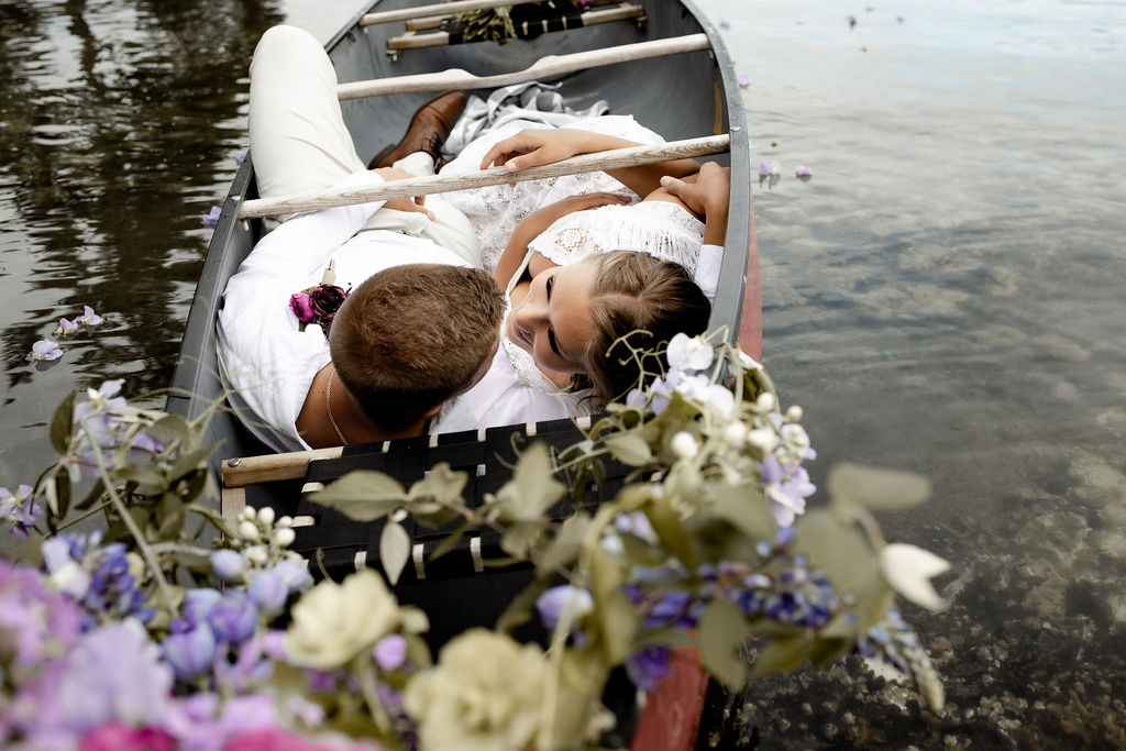 Adventure Elopement couple snuggle in the bottom of a canoe with flowers above them
