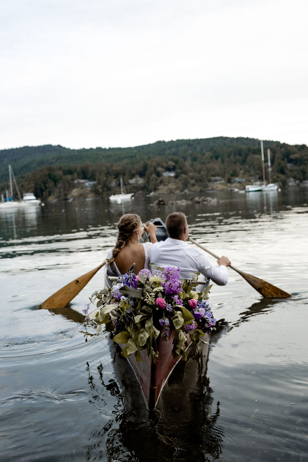 Newlyweds paddle canoe filled with purple and pink flowers on Vancouver Island